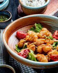 side view of fried chicken with tomatoes and sauce on lettuce on a plate on rustic background
