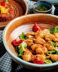 side view of fried chicken with tomatoes and sauce on lettuce on a plate on rustic background