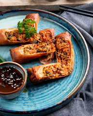side view of fried spring rolls with chicken and vegetables served with soy sauce on a plate on black background
