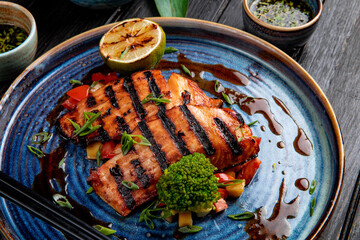 side view of grilled salmon with vegetables lemon and soy sauce on a plate on wooden table