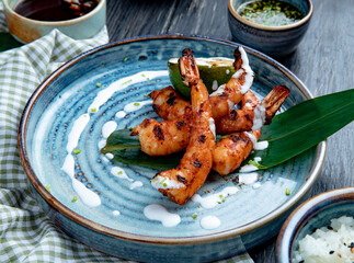 side view of grilled shrimps with sauce on a plate on wooden background