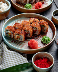 side view of hot fried sushi rolls with salmon avocado and cheese served with ginger and wasabi on a plate on wooden background