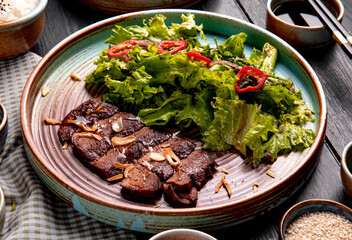side view of roasted beef with lettuce and red chili pepper on a plate on wooden background