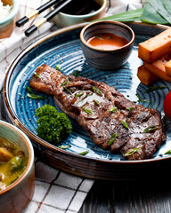 side view of roasted beef with spicy sauce and grilled tomato with fried bread sticks on a plate