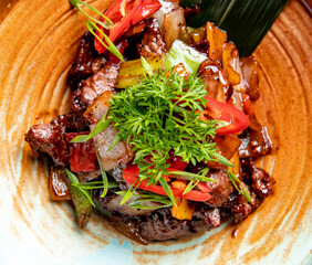 side view of roasted lamb with vegetables and fresh herbs and sauce on a plate on wooden background