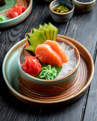 side view of salmon sashimi with sliced cucumbers  ginger and wasabi sauce on ice cubes in a bowl...