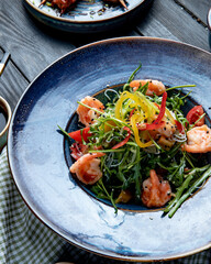 side view of shrimp salad with bell peppers and arugula on a plate on wooden background