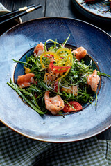 side view of shrimp salad with bell peppers arugula on wooden background