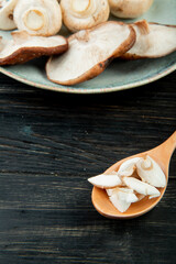 side view of sliced mushrooms in a wooden spoon and whole mushrooms on a plate on dark wooden rustic background