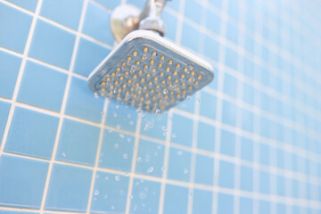 Wall mounted chrome shower on blue tiles with water drops