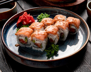 side view of sushi rolls with salmon and cream cheese  served with ginger and wasabi on a plate on wooden background