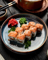 side view of sushi rolls with salmon and cream cheese  served with ginger and wasabi on a plate with soy sauce on wooden background