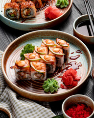 side view of sushi rolls with shrimps avocado and cream cheese served with ginger and wasabi on a plate on wooden background