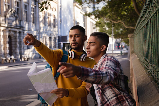 Two mixed race male friends standing in city street, looking at map, talking and pointing direction