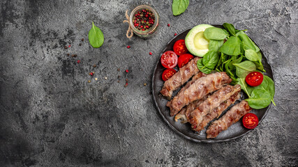 grilled sausages minced meat wrapped in bacon with with spinach, avocado and cherry tomato. chevapchichi or Kofta kebab, diet lunch concept. Keto paleo diet menu