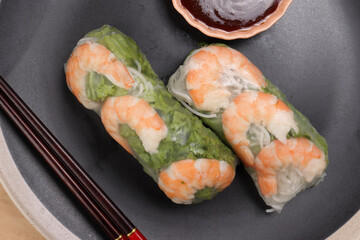 Vietnamese prawn shrimp see through rice paper spring roll green vegetable sauce on dark plate chopsticks wooden table