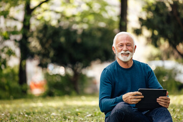 Fototapeta premium Senior man, looking through his tablet, outside.