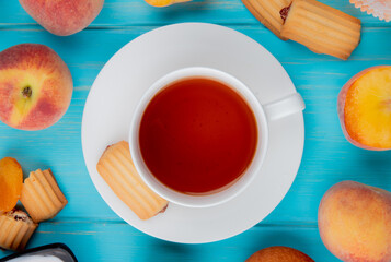 top view of a cup of tea with biscuits fresh ripe peaches and dried apricots on blue background