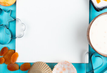 top view of a sketchbook and dried apricots cottage cheese yogurt and cookie cutters arranged on blue background