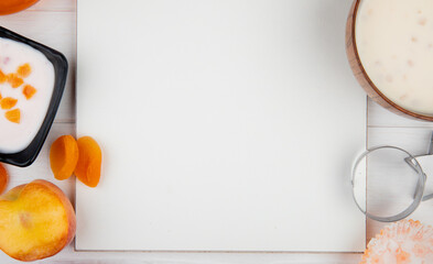 top view of a sketchbook and fresh peache dried apricots  yogurt and jam arranged around on white background