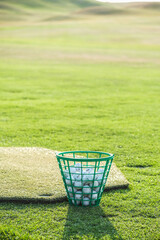 Green plastic basket with golf balls on the golf course at sunset