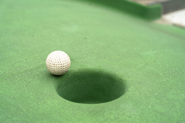 Mini golf. White ball near hole on green court. Summer outdoor game.