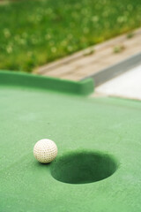 Mini golf. White ball near hole on green court. Summer outdoor game.