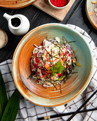 top view of chinese salad with chopped cabbage bell peppers and sea kale decorated with red caviar on a plate and soy sauce on wooden background
