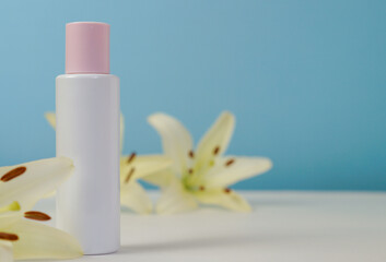 White blank cosmetic bottle with cream with pink cap, moisturizing lotion or shampoo framed with fresh lily flowers on a light blue background. Natural organic spa. Cosmetic concept. Front view.