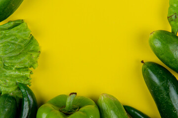 top view of frame made of fresh vegetables green chili peppers cucumbers and green chili peppers on yellow background with copy space