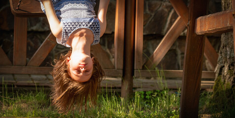 Close up portrait of beautiful young girl sitting on the swing upside down. Concept of childhood and happiness. Copy space for text or design.