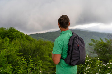 Traveler in green T-shirt with gray backpack, enjoying view of rain clouds in hills. Calm in mountains before thunderstorm