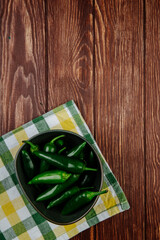 top view of fresh green chili peppers in a bowl on plaid napkin on wooden rustic background with copy space