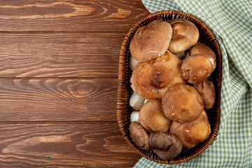 top view of fresh mushrooms in a wicker basket and plaid fabric on wooden rustic background with copy space