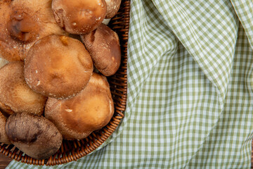 top view of fresh mushrooms in a wicker basket on plaid fabric background with copy space