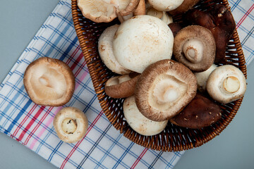 top view of fresh mushrooms in a wicker basket on plaid napkin on light blue background