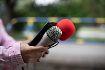 Professional journalist at event, holding microphones and recording notes on smartphone