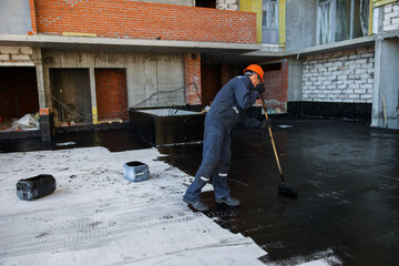 Waterproofing coating. A worker applies bitumen mastic to the foundation. Roofer cover the waterproofing primer on the roof, modified with polymer bitumen, with a roller brush.
