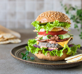 Tasty fresh homemade beef burger with cheese, salad and vegetables on ceramic plate. Street food. Fast food and junk food concept.