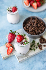 Healthy breakfast or dessert with natural yogurt, chocolate granola and strawberries, blue concrete background.