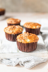 Tasty breakfast muffins with oat crumbs topping on white cutting board, light concrete background.