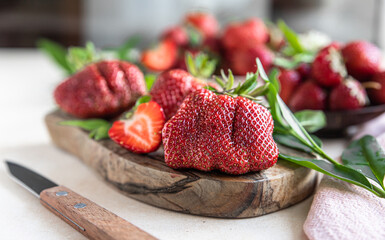 Ugly organic strawberries on wooden cutting board. Organic strawberries of unusual shape. Trendy...
