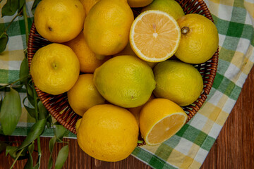 Fototapeta na wymiar top view of fresh ripe lemons in a wicker basket with green leaves on plaid fabric background