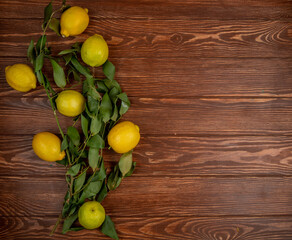 top view of fresh ripe lemons with green leaves on on rustic wooden background with copy space