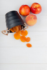 top view of fresh ripe nectarines and dried apricots scattered from small bucket on white background