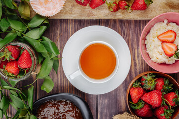 top view of fresh ripe strawberries with jam cottage cheese and a cup of tea on rustic wooden background