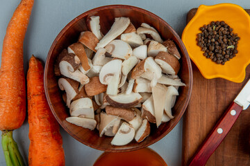 top view of fresh sliced mushrooms in a bowl and kitchen knife with black peppercorns on a wooden...