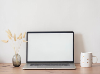 Home office desk with open laptop, dry autumn branches in vase and white mug