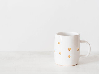 Ceramic cup with gold stars, minimal Christmas decoration and on white background.