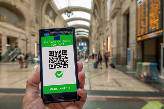 Woman showing on smartphone EU Digital Covid Certificate with quad code. Railway station background.